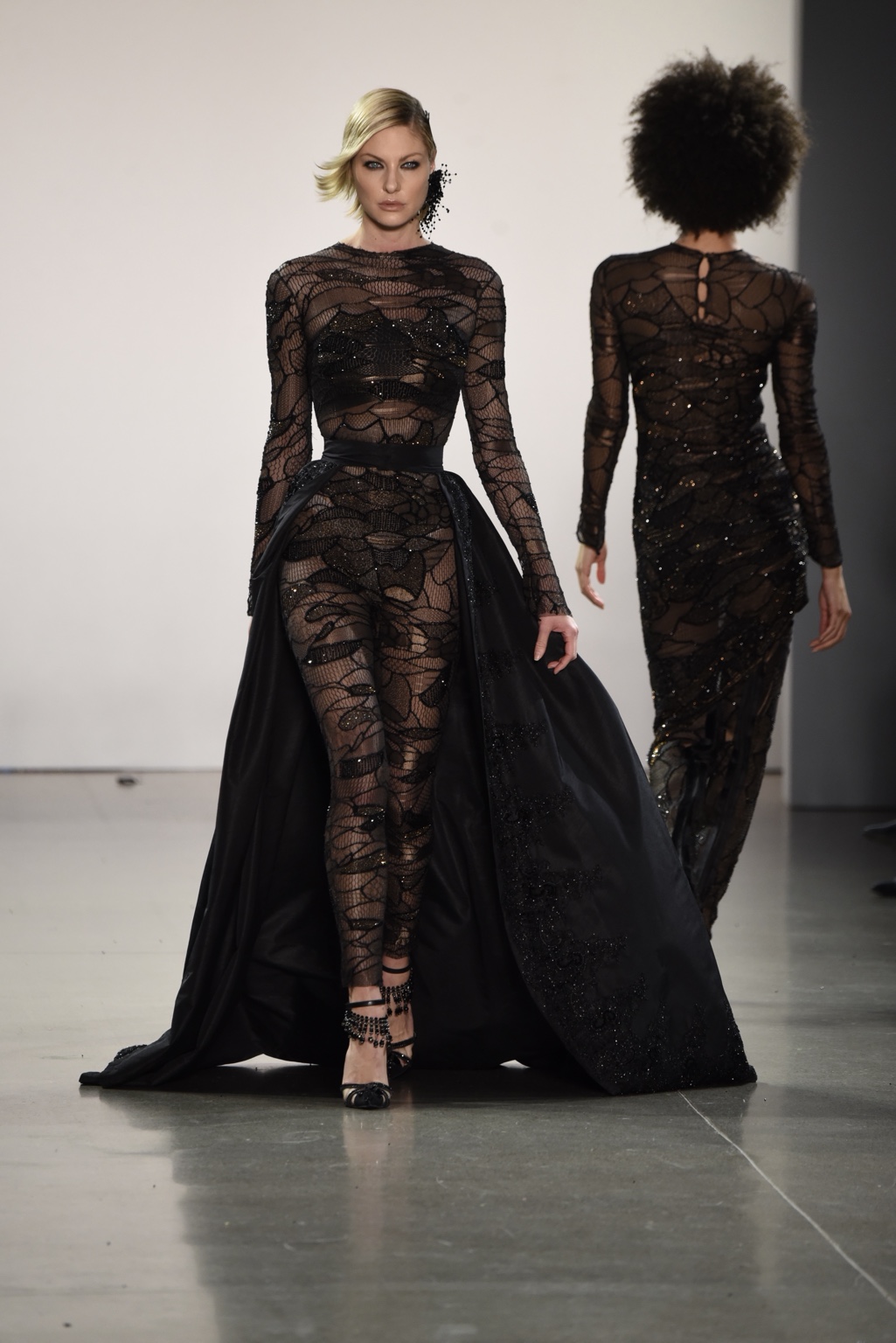 Model walking forward in a black lace runway gown