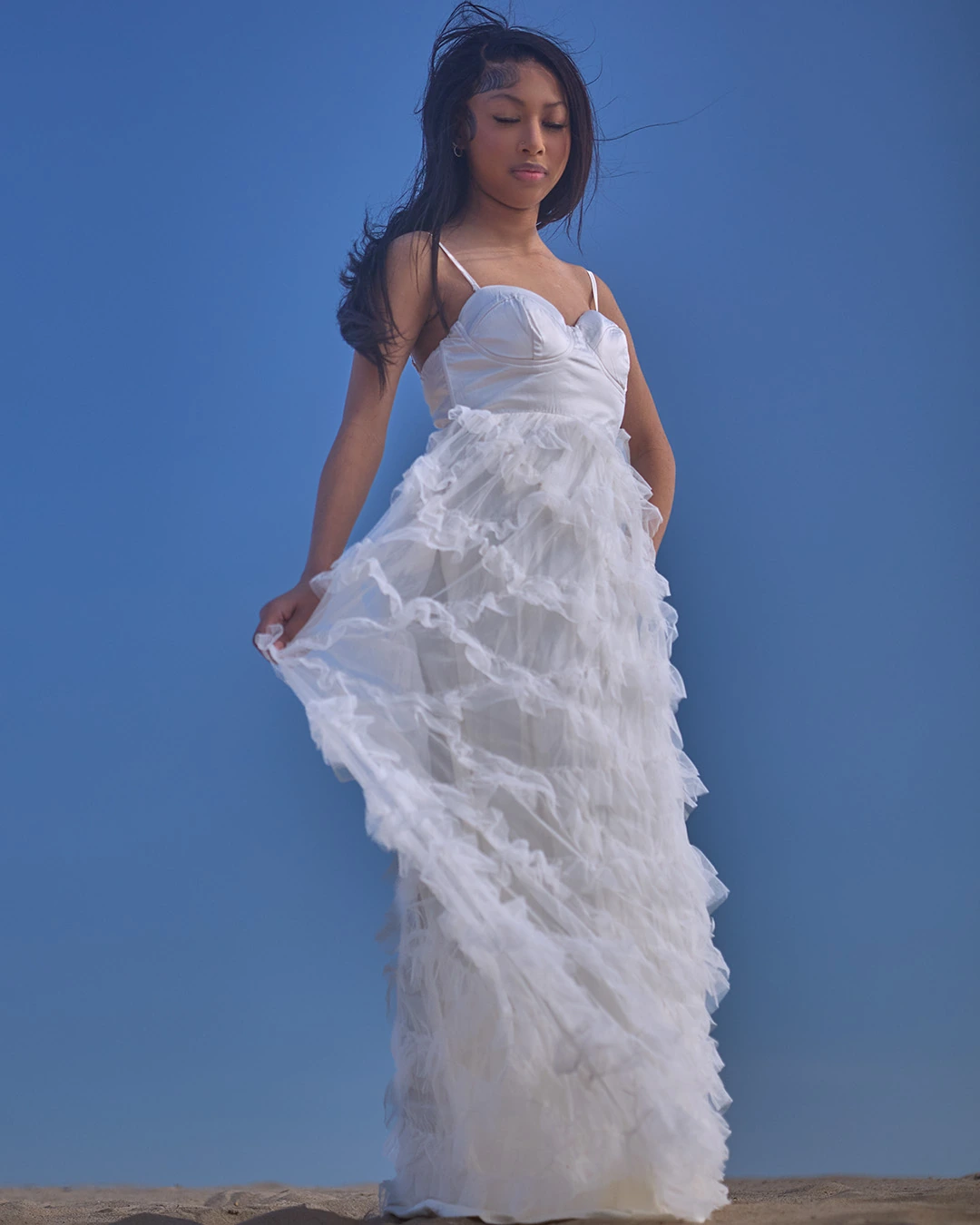Young model in a white ruffled gown against a blue sky