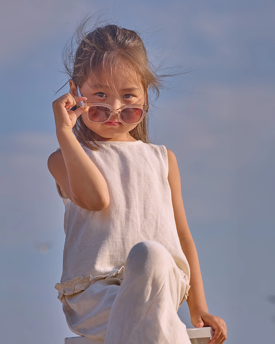 Young model in sunglasses and a light outfit seated on a stool