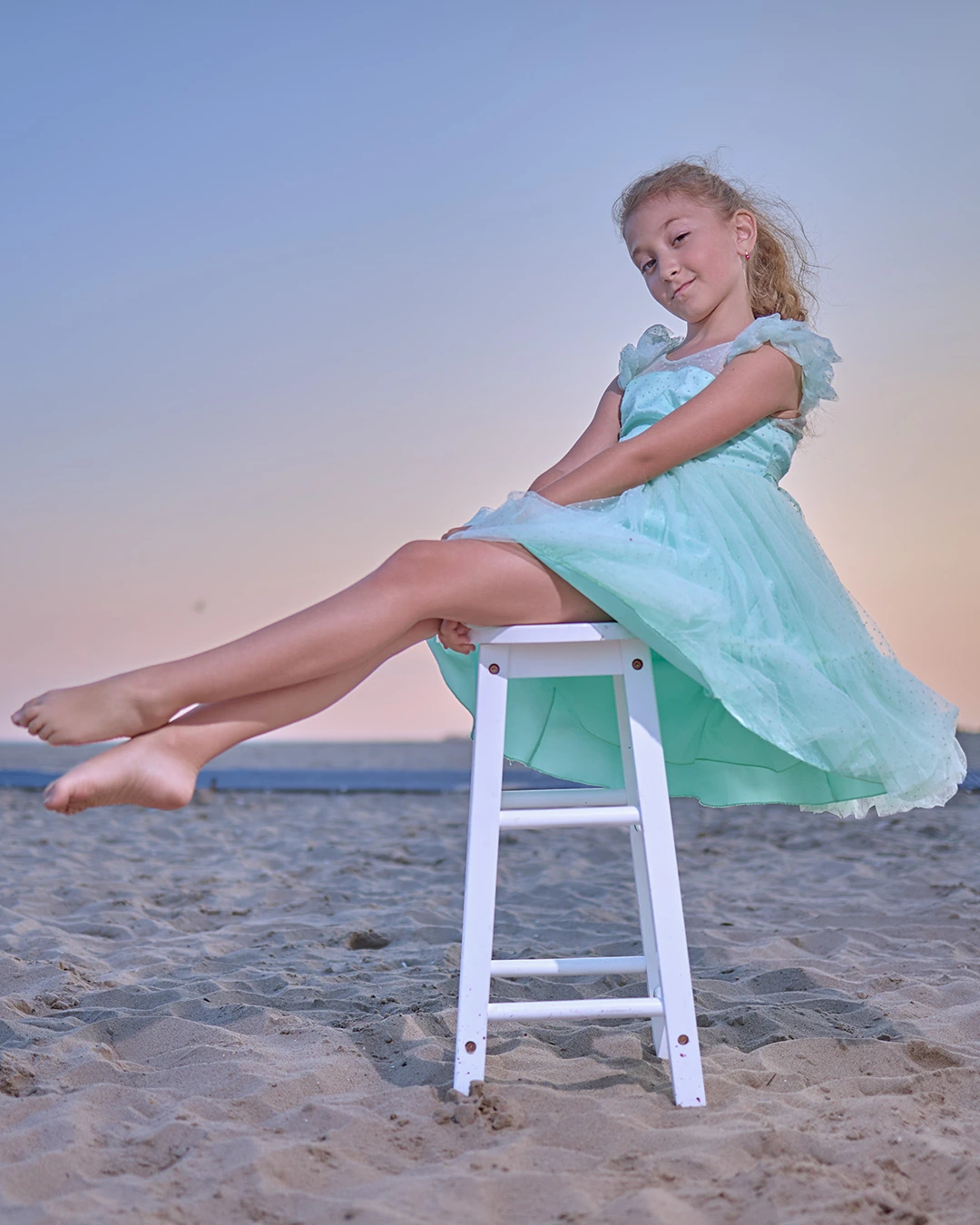 Young model in a mint dress seated on a white stool at the beach